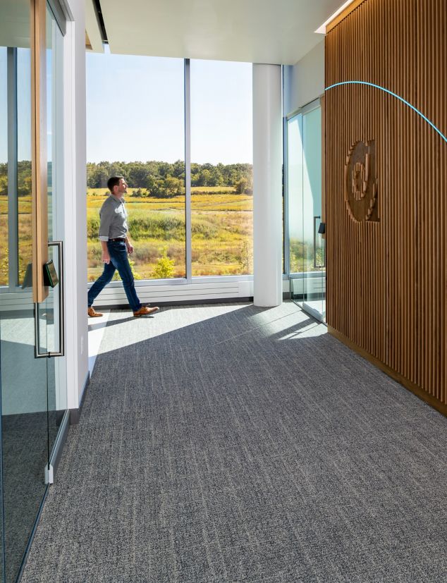 Interface Open Air 401 plank carpet tile in corporate corridor with wood panel wall and glass exterior wall
