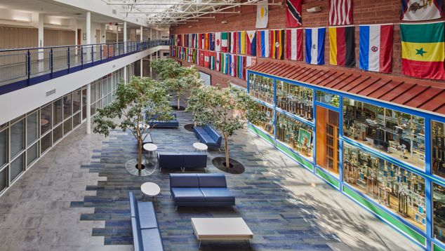 Interface Reclaimed plank carpet tile and Textured Stones square LVT in open K-12 atrium with trees and colorful flags