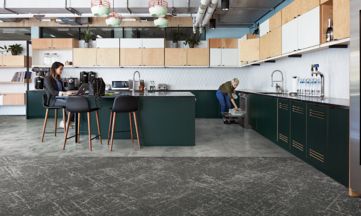 Interface Ice Breaker carpet tile and Textured Stones LVT in kitchen area with women lodaing dish washer and women working on computer