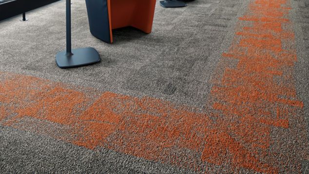 Interface Open Air 404 carpet tile in corner space with open cement ceiling and orange chairs