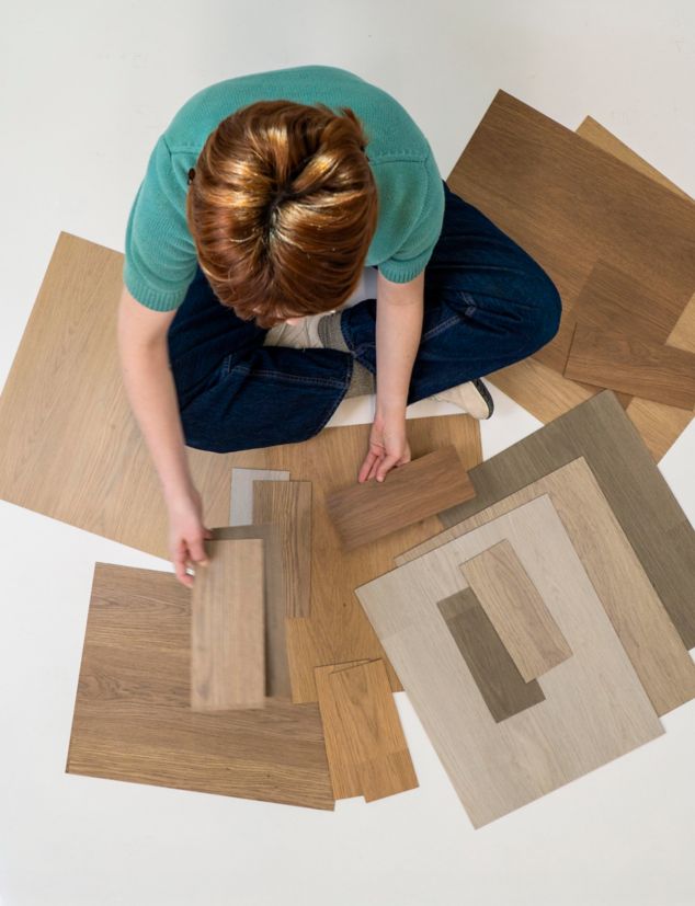 woman sitting cross-legged looking at different color samples of noravant timber rubber flooring